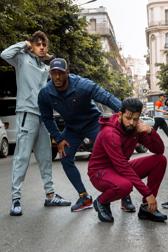 gallery-01 Three men pose in stylish active wear on a city street, embodying modern urban fashion.